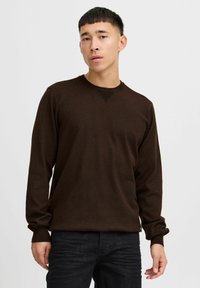 Suéter de punto marrón con mangas largas, cuello redondo y acentos de canalé en el escote y los puños. Textura suave y corte clásico.