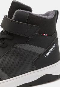Sneaker alta nera con superficie testurizzata, dettagli grigi, cinturino in velcro e suola bianca; presenta il logo del brand e colletto imbottito.