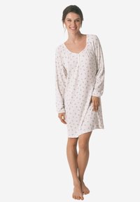 Camicetta da notte bianca a maniche lunghe con texture a coste, caratterizzata da un delicato motivo floreale e un collo a barca. Lunghezza fino a metà coscia.