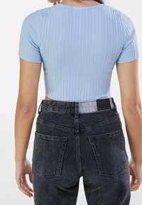 T-shirt cropped a coste blu chiaro con maniche corte, abbinata a jeans in denim neri a vita alta con tasche posteriori e una cintura a contrasto.