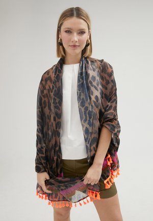 Kimonový kimono s leopardím potiskem z průsvitné látky, se oranžovými střapci podél lemu, vrstvený přes bílé tričko a olivové kraťasy.