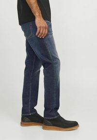 Jeans din denim albastru închis cu croi drept, cusături discrete și un accent roșu pe buzunarul din spate. Asortați cu pantofi casual negri.