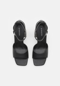 Sandales à talons hauts noires avec un bout carré, dessus en cuir lisse, dos ouvert et bride de cheville avec accent en métal argenté.