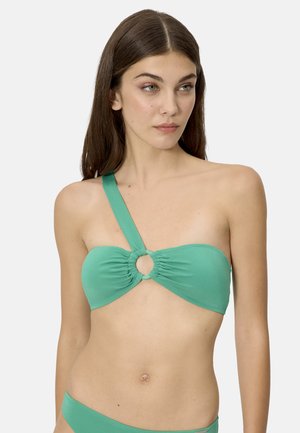 Mujer con un bikini verde de un solo hombro con un detalle de anillo central y parte inferior a juego, sobre un fondo liso.