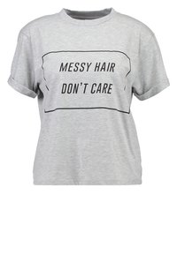 Camiseta de algodón gris con mangas enrolladas, que presenta un gráfico rectangular negro con la frase "CABELLO DESORDENADO NO ME IMPORTA" en letras negritas.