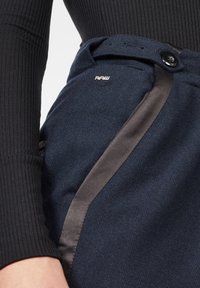 Mörkblå tygkjol med en satin svart accent på sidan. Inkluderar en knappstängning och en liten silverfärgad logodetalj.