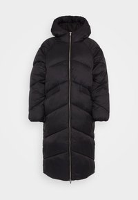 Lång svart pufferjacka med hög krage, med dragkedjestängning och chevronquiltat mönster. Tillverkad av mjukt, lättviktigt material.