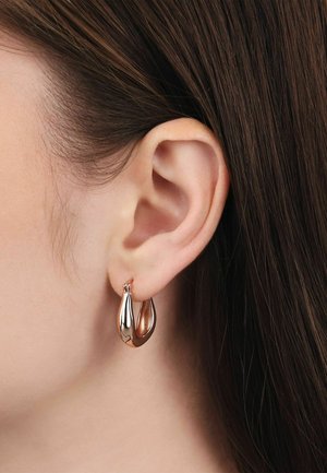 Nahaufnahme eines linken Ohrs mit glattem braunen Haar und einem kleinen, glänzenden goldenen Creolenohrring.