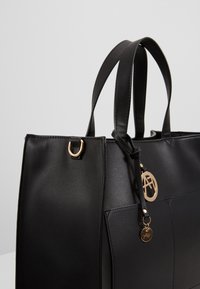Sac cabas en cuir noir avec deux poignées, détails en métal doré et une étiquette logo. Présente une forme structurée et une texture lisse.
