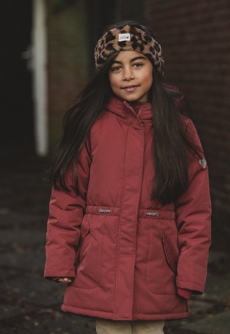 Rode gewatteerde jas met verstelbare taille, zijzakken en een bruine luipaardprint hoofdband. Lange donkere haren en een neutrale achtergrond.