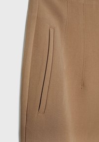 Gros plan d’un vêtement beige montrant une poche à fente verticale avec des coutures nettes sur un tissu lisse.