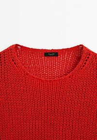 Pull rouge en maille avec un col large, un motif ajouré et une finition texturée. Étiquette visible au niveau du col.