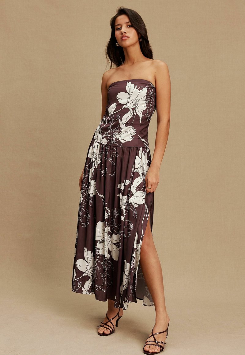 Rochie maro cu imprimeu floral alb fără bretele, din material vaporoasă, cu fenta laterală și corsaj ajustat. Asortată cu sandale negre cu barete.