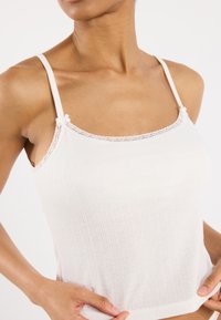 Light pink ribbed camisole with delicate lace trim around the neckline, adjustable straps, and a fitted silhouette.