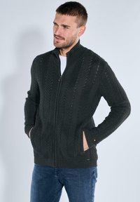 Dunkelgrauer Reißverschluss-Pullover mit strukturiertem Chevron-Muster, hoher Kragen und seitlichen Taschen, aus dicker Strickware gefertigt.