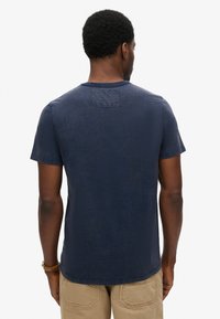 Marineblaue kurzärmelige T-Shirt mit Rundhalsausschnitt und einem rechteckigen Patch auf dem Rücken. Hergestellt aus strukturiertem Stoff, ausgelegt für eine lässige Passform.
