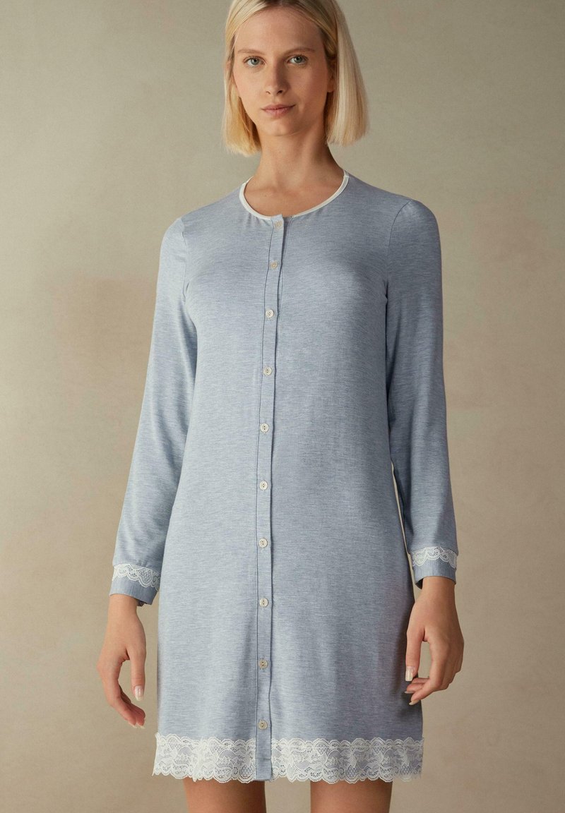 Ljusblå nattklänning med knappar, tillverkad av mjukt tyg, med långa ärmar och vit spetskant vid ärmsluten och nederkanten.