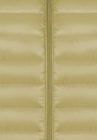 Primo piano di un tessuto beige trapuntato con zip centrale, che mostra cuciture orizzontali e una superficie sintetica liscia.