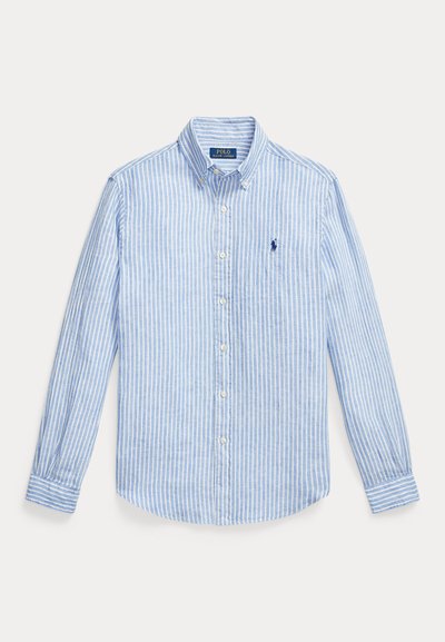 Ανοιχτό μπλε και λευκό πουκάμισο με κάθετες ρίγες, μακριά μανίκια, κούμπωμα με κουμπιά και γιακά με κουμπιά. Έχει κεντημένο ναυτικό λογότυπο στο στήθος.