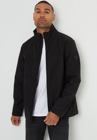Schwarze Softshelljacke mit hohem Kragen, Reißverschluss vorne und zwei Seitentaschen. Mit einem dezenten Logo auf dem linken Ärmel.