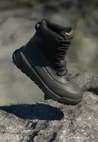 Μαύρο αδιάβροχο μποτάκι με ψηλό σχέδιο, υφή στο πάνω μέρος, ανθεκτικά κορδόνια και σόλα κατάλληλη για σκληρές επιφάνειες. Ιδανικό για εξωτερικούς χώρους.