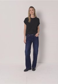 Czarna bluzka z krótkim rękawem zestawiona z ciemnoniebieskimi dzwonami. Jeansy mają klasyczny fason z pięcioma kieszeniami i gładką teksturę denimu.
