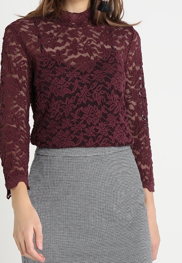 Bordeaux spetsblus med långa ärmar och hög krage, prydd med blommönster. Bärs över en grå rutmönstrad kjol. Genomskinlig textur.