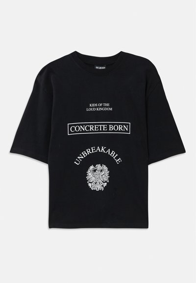 Svart oversized T-skjorte med hvit tekst "Kids of the Loud Kingdom," "Concrete Born," "Unbreakable," og et detaljert ørner Graphic under.