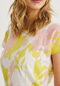 Bavlněné tričko s krátkým rukávem s květinovým vzorem v růžové a limetkové barvě na bílém pozadí. Kolo výstřih a uvolněný střih.