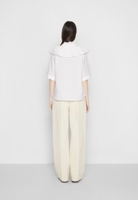 Chemise blanche avec un col montant froufroué, manches courtes et coupe carrée, associée à un pantalon large crème taille haute.