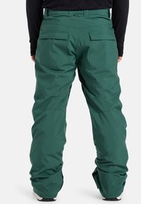 Grüne Schneehosen mit lockerem Schnitt, ausgestattet mit Gesäßtaschen und Reißverschlüssen an den Knöcheln. Hergestellt aus einem wetterbeständigen Material.