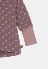 Fleece-Oberteil in hellem Mauve mit beigen Punkten. Verfügt über lange Ärmel mit einem einfarbigen Mauve-Bündchen und einem kleinen Markenetikett am Saum.