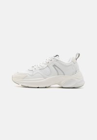 Hvid atletisk sneakers med en struktureret mesh-overdel, polstret krave og en chunky sål. Fremhævet af metalliske snørehuller og en plysbånd.