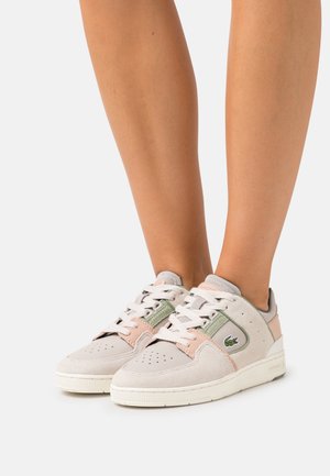 Baskets en daim gris avec des accents rose pâle et vert. Dotées d'un embout perforé, d'une semelle en caoutchouc blanche et du logo Lacoste sur le côté.