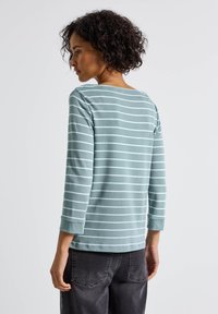 Mintgrünes Langarmshirt mit weißen horizontalen Streifen, Rundhalsausschnitt und gerippten Bündchen. Kombiniert mit dunkelgrauen Hosen, die eine lockere Passform zeigen.