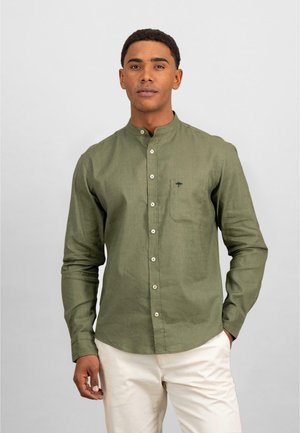 Olijfgroene lange mouwen shirt met een staande kraag, voorzak en witte knopen; gemaakt van gestructureerde stof. Model draagt lichtgekleurde broek.