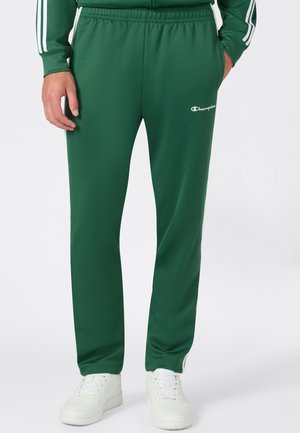 Parte inferiore del corpo con pantaloni sportivi verdi Champion con vita elastica e scarpe da ginnastica bianche su sfondo uniforme.
