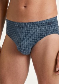 Blaue Schwimmslips mit einem geometrischen Diamantenmuster in hellen und dunklen Farbtönen. Hergestellt aus glattem Stoff mit einem sicheren Bund.