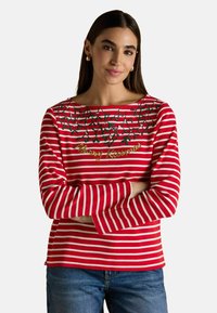 Czerwona i biała koszula z długim rękawem w paski, z okrągłym dekoltem, haftowanym zielonym jemiołą oraz napisem "Merry Kissmas" w złotym kolorze.