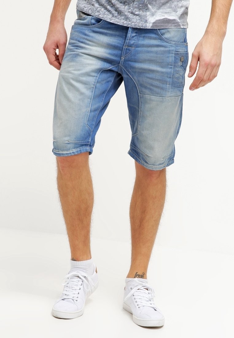 Vaaleansiniset farkkuhousut, joissa on haalistunut pinta. Ominaisuuksiin kuuluvat käänteet, etutaskut ja lisätasku sivulla. Yhdistetty valkoisiin lenkkareihin.