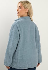 Giacca in pile azzurro chiaro con superficie testurizzata e morbida. Presenta un colletto e maniche lunghe, progettata per una vestibilità comoda.