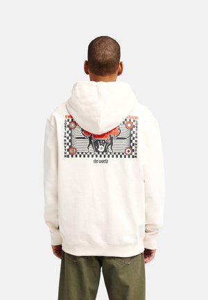 Persoon draagt een witte hoodie met een rood, zwart en wit grafisch ontwerp van twee silhouetten en tekst op de achterkant.