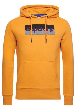 Orange hooded sweatshirt with front kangaroo pocket and black-and-gray patch displaying the word "Superdry" in maroon letters.