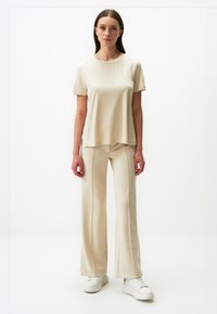 Beżowa bluzka z krótkim rękawem i okrągłym dekoltem, w zestawieniu z szerokimi spodniami w dopasowanym kolorze, gładka faktura materiału i minimalistyczny design.