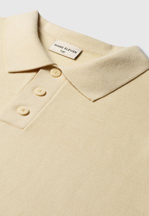 Lichtbeige polo shirt met ribbelstructuur, drie knoopsluiting en een zachte kraag. Etiket leest "HANG ELEVEN" en maat "Groot."