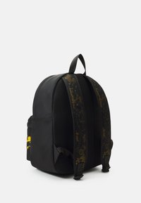 Sac à dos noir avec des panneaux latéraux en mailles, des accents jaunes et une poignée supérieure. Dispose de bretelles rembourrées pour le confort et d'une conception structurée.
