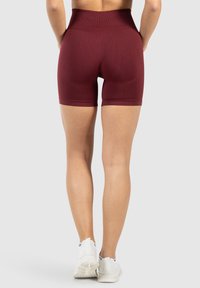 Bordowe szorty sportowe z wysokim stanem, elastyczny materiał o gładkiej fakturze, w długości do połowy uda i minimalnymi szwami.