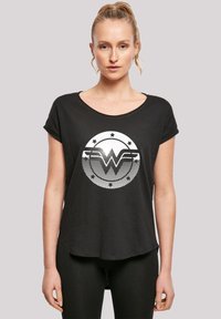 Musthave musta lühikese varrukaga T-särk ümmarguse kaelusega, millel on valge Wonder Womani logo ja tähed ringikujulises disainis. Pehme kangas.