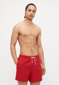 Shorts de bain rouges avec une taille élastique et un cordon blanc. Tissu lisse avec une coupe décontractée et des poches latérales.