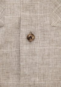 Tissu à carreaux beige et blanc avec un seul bouton marron à quatre trous cousu au centre.